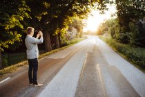 Мужчина фотографирует дорогу на смартфоне на закате — стоковое фото