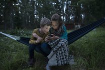 Хлопчик і дівчинка в гамаку дивлячись на стільниковий телефон — стокове фото
