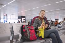 Seniorin schreibt SMS am Flughafen, Menschen im Hintergrund — Stockfoto