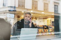 Homem falando no telefone inteligente por laptop atrás da janela — Fotografia de Stock