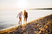 Vista trasera de dos mujeres caminando en la playa - foto de stock