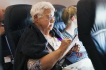 Жінка робить кросворд на літаку, фокус на передньому плані — стокове фото