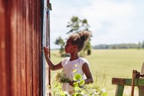 Girl holding flowers by barn, focus on foreground — Stock Photo