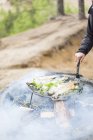 Cropped view of man cooking fish over campfire, selective focus — Stock Photo