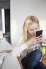 Mensajes de texto chica en el teléfono inteligente en la sala de estar - foto de stock