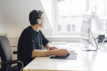 Чоловік в навушниках і використовує комп'ютер в офісі — стокове фото