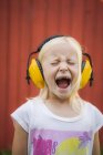 Portrait of blonde girl wearing ear muffs, screaming with eyes closed — Stock Photo