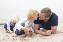 Dos chicos pasando tiempo con el hombre en la playa - foto de stock
