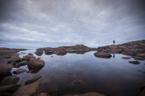 Woman standing by rock pool under overcast sky — Stock Photo