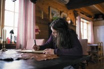Giovane donna seduta a tavola e che scrive in latticini — Foto stock