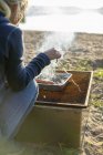 Cropped view of woman cooking barbecue by lake — Stock Photo