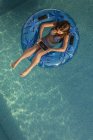 Menina flutuando no anel na piscina e usando tablet digital — Fotografia de Stock