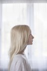 Side view of blonde girl in front of white curtains — Stock Photo