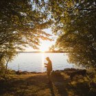 Середній дорослий чоловік стоїть з вудкою на річці на заході сонця — стокове фото