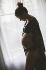 Беременная женщина в нижнем белье стоит у окна — стоковое фото