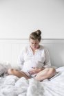 Беременная женщина сидит на кровати и смотрит вниз — стоковое фото