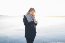 Mulher usando telefone inteligente por mar — Fotografia de Stock