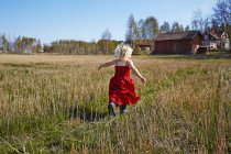 Girl wearing red dress running in field, Runnas — Stock Photo
