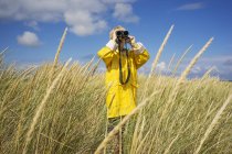 Boy in wet weather gear looking through binoculars — Stock Photo