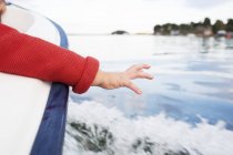 Cropped view of child reaching for water from boat — Stock Photo