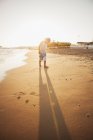 Menino em roupas casuais andando na praia ao pôr do sol — Fotografia de Stock