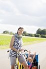 Mãe de ciclismo com a jovem filha em reboque de bicicleta — Fotografia de Stock