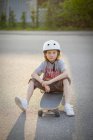 Portrait of boy sitting on skateboard on street — Stock Photo