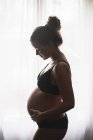 Вид сбоку на беременную женщину, стоящую у окна — стоковое фото