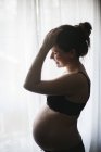 Vista lateral da mulher grávida em pé pela janela — Fotografia de Stock