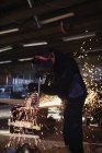 Jeune homme coupant du métal en atelier — Photo de stock