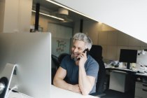 Mann spricht am Schreibtisch mit Smartphone, Fokus auf Vordergrund — Stockfoto