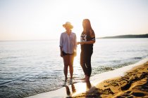 Дві жінки, що стоять на пляжі на заході сонця — стокове фото