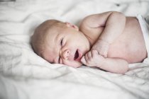 Newborn baby boy lying on bed, focus on foreground — Stock Photo