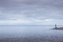 Femme debout sur des rochers par la mer sous un ciel couvert — Photo de stock