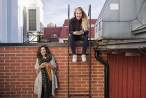 Deux jeunes femmes utilisant des téléphones intelligents sur le toit — Photo de stock