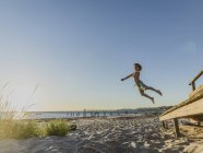 Boy in swimsuit at beach jumping into sand — Stock Photo