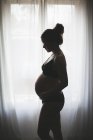 Вид сбоку на беременную женщину, стоящую у окна — стоковое фото