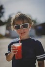 Kleiner Junge mit Sonnenbrille trinkt matschig, Fokus auf Vordergrund — Stockfoto