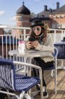 Молодая женщина, используя смартфон, сидя за столом — стоковое фото