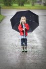 Girl standing in rain with umbrella, focus on foreground — Stock Photo