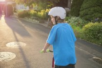 Вид сзади на мальчика на скутере вдоль городской улицы — стоковое фото