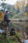 Homem com cão preto pesca no rio — Fotografia de Stock