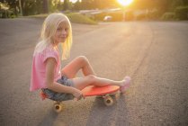 Portrait de fille assise sur un short-board rouge dans la rue — Photo de stock