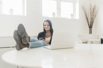 Женщина с ногами на белом столе за ноутбуком — стоковое фото