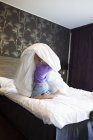 Girl playing with blanket in hotel bedroom — Stock Photo