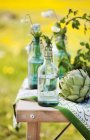 Flowers in bottles and artichoke on table, selective focus — Stock Photo