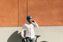 Чоловік стоїть з велосипедом і розмовляє на смартфоні — стокове фото