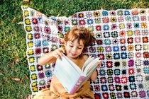 Mädchen liest Buch auf Picknickdecke — Stockfoto