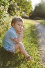 Маленький хлопчик, сидячи на траві, зосередити увагу на передньому плані — стокове фото
