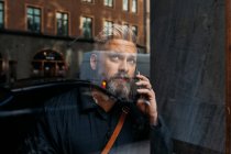 Homem em telefone inteligente através da janela — Fotografia de Stock